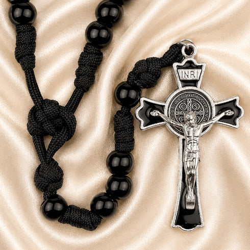 Black beaded rosary with a silver crucifix pendant on a draped champagne satin background.