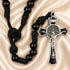 Black beaded rosary with a silver crucifix pendant on a draped champagne satin background.
