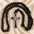 Black beaded rosary with a black and silver cross, on a beige satin fabric background.