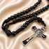 A black beaded rosary with a black cord and a silver crucifix, on a beige satin fabric background.