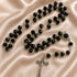 A black bead rosary with silver-tone chain links, a round centerpiece, and a silver crucifix, on a champagne fabric background.