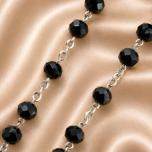 Faceted black beads connected by silver-toned chain links, on a champagne satin fabric background.