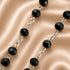 Faceted black beads connected by silver-toned chain links, on a champagne satin fabric background.