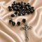 Black faceted bead rosary with a silver-tone crucifix and centerpiece, arranged on draped champagne satin fabric.