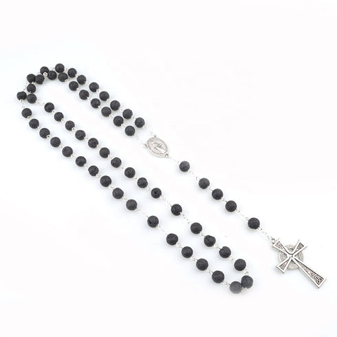 Black lava stone rosary with silver Celtic cross and Miraculous medal on a white background.