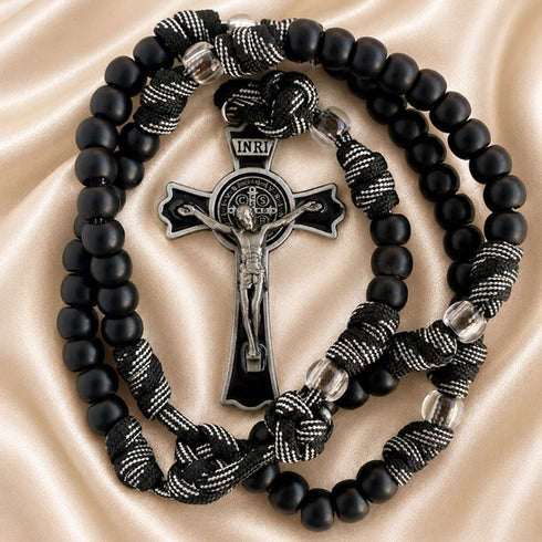 Black beaded rosary with a silver-toned crucifix and black-and-white knotted cord, on a beige satin.