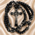 Black beaded rosary with a silver-toned crucifix and black-and-white knotted cord, on a beige satin.
