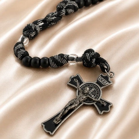 A black and silver crucifix rosary with knotted cord and matte black beads, on a beige fabric background.