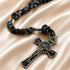 A black and silver crucifix rosary with knotted cord and matte black beads, on a beige fabric background.