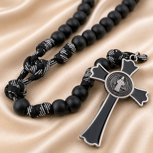 Black beaded rosary necklace with a black and silver cross, on a beige satin fabric background.