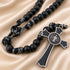 Black beaded rosary necklace with a black and silver cross, on a beige satin fabric background.