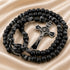 Black beaded rosary with a silver-toned crucifix and black-and-white knotted cord, on a satin fabric background.