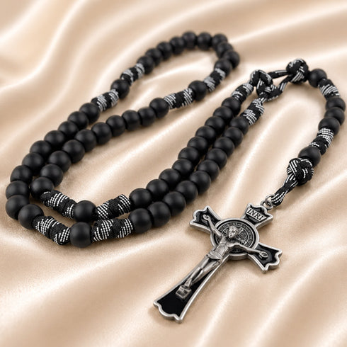 A black beaded rosary with silver-toned metal accents, a black crucifix, on a satin fabric background.