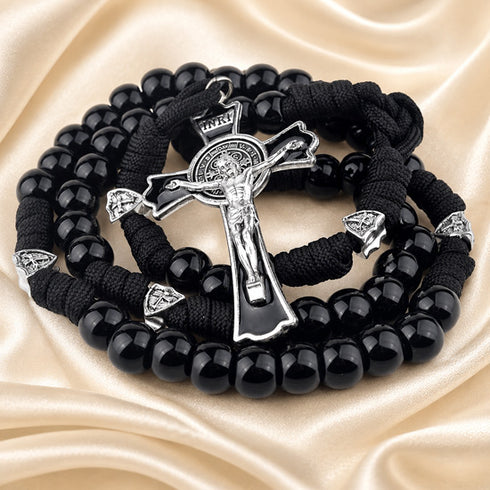 A black beaded rosary with a silver-tone crucifix, displayed on draped satin fabric.