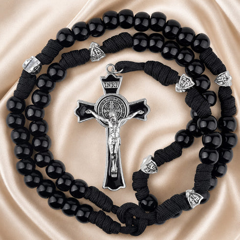 Black rosary with a silver crucifix and silver heart-shaped spacer beads, on a beige background.