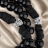 A close-up of a black rosary with glossy round beads, black cord, and two silver-toned shield-shaped charms featuring a cross design.