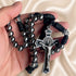A close-up of a hand holding a rosary with metallic beads, black cord, and a silver-toned crucifix on a cream satin fabric.
