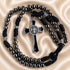 A black beaded rosary with a black cord, featuring a silver-toned crucifix on a beige satin fabric background.