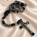 A gothic-style black and silver rosary with a crucifix, on a draped fabric background.