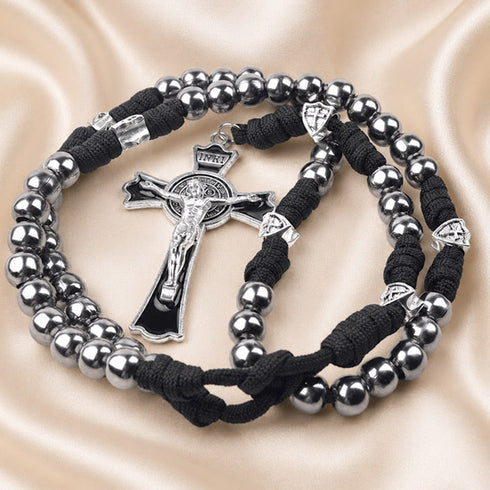 A black and silver rosary with a crucifix, arranged on a beige satin fabric background.