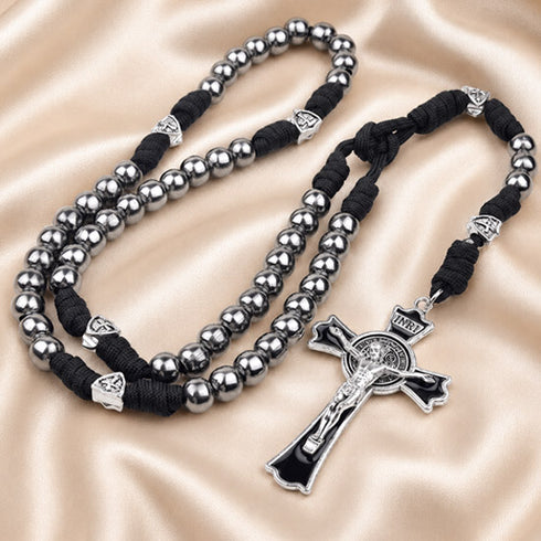 A black and silver rosary with black braided cord, metallic silver beads, and a black cross pendant, on a beige background.