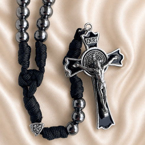 Black cord rosary with metallic silver beads and a silver crucifix, on a beige satin background.