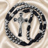 A black and silver rosary with metallic beads, a crucifix, and small heart-shaped charms, on a satin fabric background.