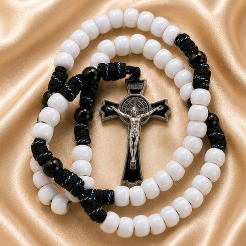 A Catholic rosary with white beads, blue cord, and a silver-tone crucifix, on a draped satin fabric background.
