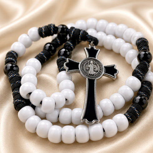 A rosary with white and black beads, a black-and-silver crucifix, on a beige satin fabric background.