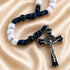 A Catholic rosary with white and black beads, dark blue knotted cord, and a silver-toned metal crucifix with enamel inlay.