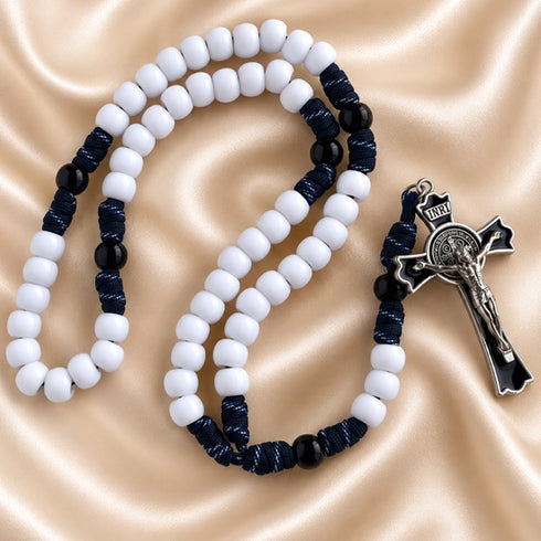 A Catholic rosary with white and black beads, blue cord and a black crucifix, on a beige fabric background.