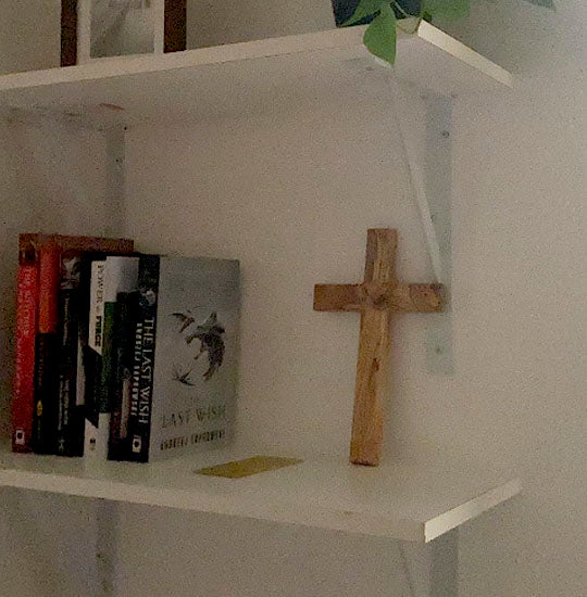 Olive Wood Thorn Cross laid on a shelf next to some books.