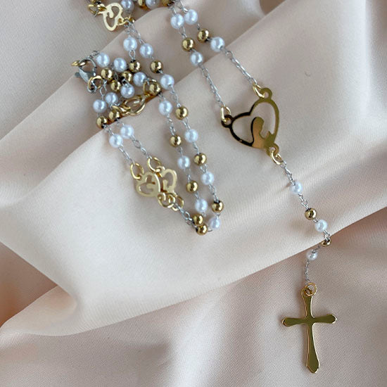 Elegant white pearl rosary with gold cross and engraved heart charm on a pink cloth.