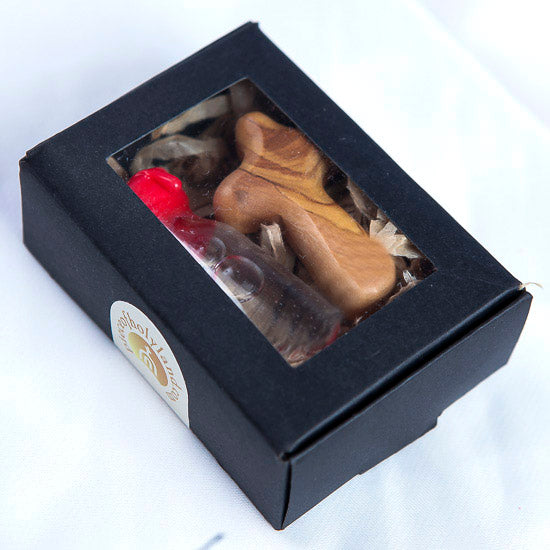 A black box containing a glass vial of Holy Water and an olive wood comfort cross, sealed with a red cap.
