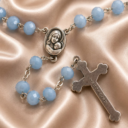 A rosary with blue beads and silver-tone metal links, featuring an oval medallion of the Virgin Mary holding baby Jesus and a cross engraved with 'JERUSALEM'.
