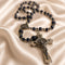 A dark blue lapis lazuli rosary with silver-toned metal beads, a St Benedict medallion, and a crucifix, on a beige satin background.