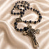 A dark blue lapis lazuli rosary with silver-toned metal beads, a St Benedict medallion, and a crucifix, on a beige satin background.