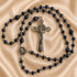 A blue beaded rosary with a silver crucifix and medallion, arranged on a beige satin fabric background.