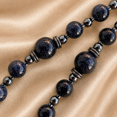 A close-up of a strand with glossy dark blue-black round beads speckled with gold glitter, separated by small metallic spacer beads.