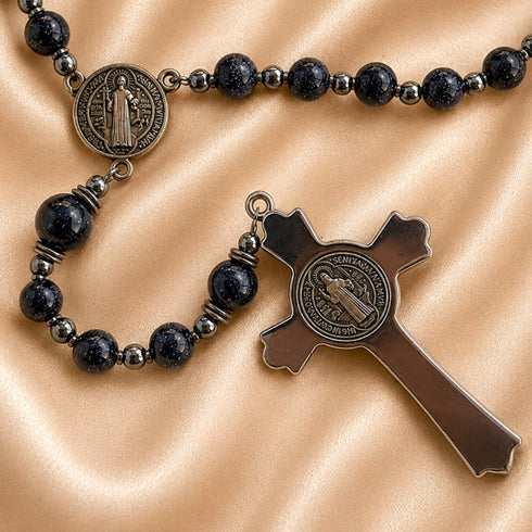 A close-up of a rosary on a satin fabric background. The rosary with dark beads, a metallic silver spacer beads and antique bronze-toned.