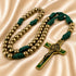 A rosary with gold-colored metal beads, dark green knotted cord, and a gold crucifix with green enamel details.