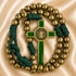 A St Benedict rosary with metallic gold beads and a green and gold cross, on a beige satin background.