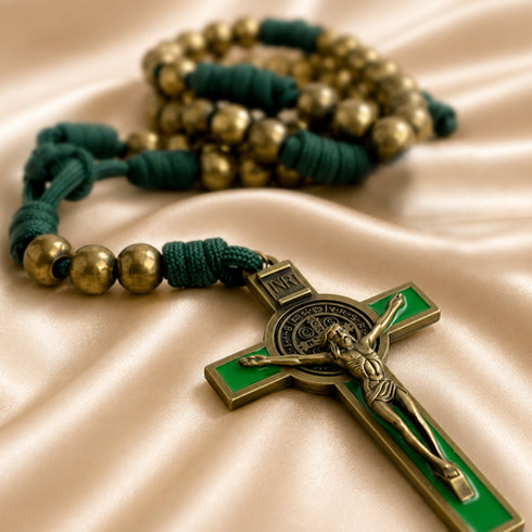 A close-up of a St. Benedict rosary featuring dark green cord, metallic gold beads, and a St.