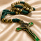 A close-up of a St. Benedict rosary featuring dark green cord, metallic gold beads, and a St.