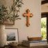 Wooden cross on a wall with decorative items like books, a vase, and a plant.