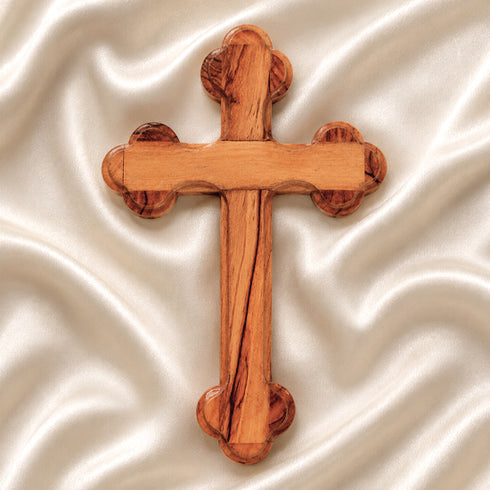 Hand-crafted olive wood budded cross from Bethlehem with carved edges, laid on white surface.