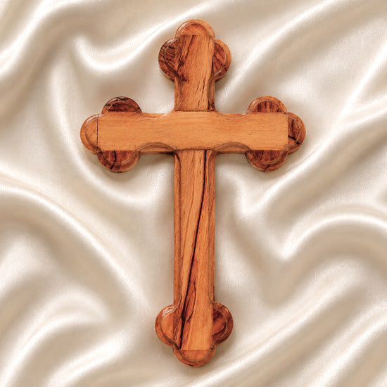 Hand-crafted olive wood budded cross from Bethlehem with carved edges, laid on white surface.
