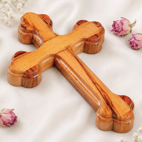 Small handmade olive wood Eastern cross with carved edges, photographed on white with rose petals.