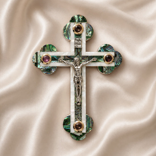 Budded olive wood cross with crucifix, white and green Mother of Pearl inlay, lying on white background.