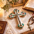 Decorative cross with Nacre on a table with a candle, books, and rosary.